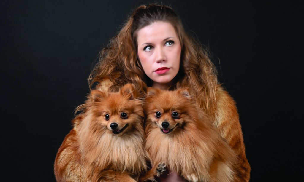 Junge Frau mit Pelzjacke hält zwei kleine Hunde im Arm mit derselben Pelzfarbe wie ihre Jacke.